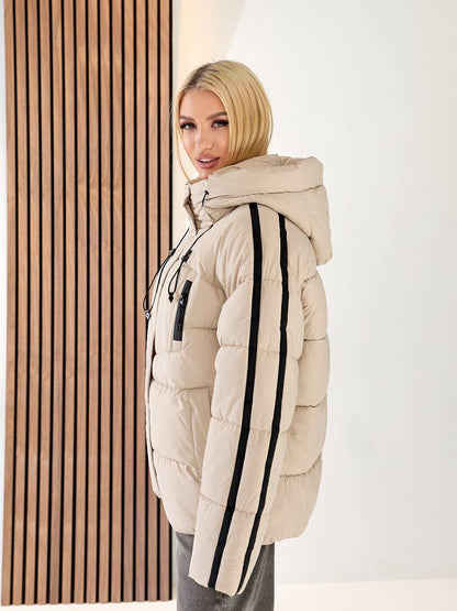 Woman wearing a beige puffer jacket with black stripes indoors.