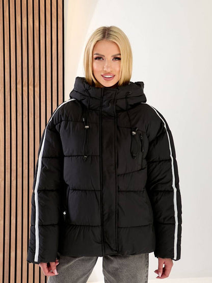 Woman wearing a black puffer jacket with white stripes on a plain background
