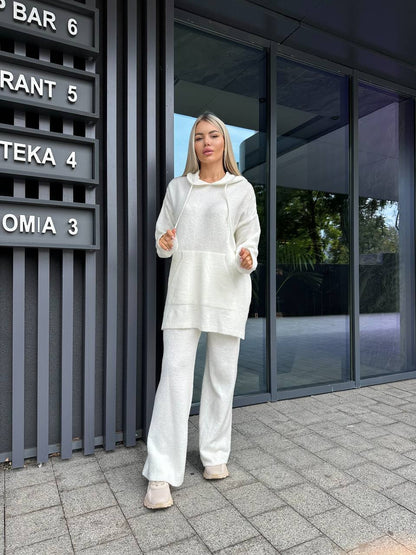 Woman in a white outfit standing outside a modern building with glass doors.
