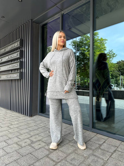 Woman in a gray tracksuit standing outside a modern building with glass doors.