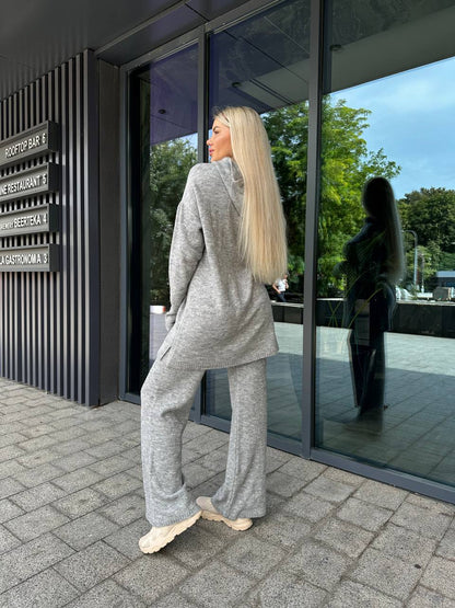 Woman in a gray outfit standing outside a building with large glass windows.