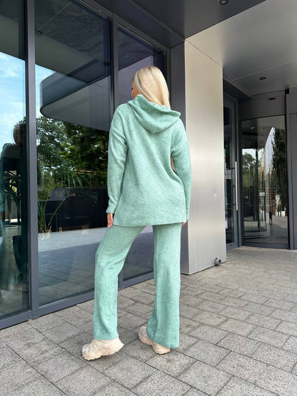 Person wearing a light green tracksuit standing outside a modern building.
