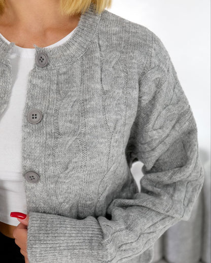 Gray cable knit cardigan worn over a white shirt with a blurred background