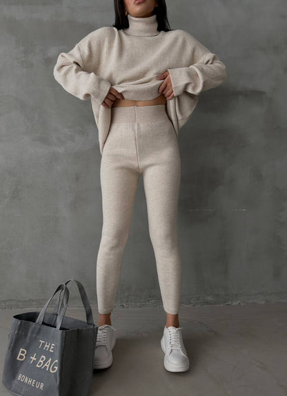 Person wearing a beige knit sweater and pants with a gray bag labeled 'B+Bag' on a gray background