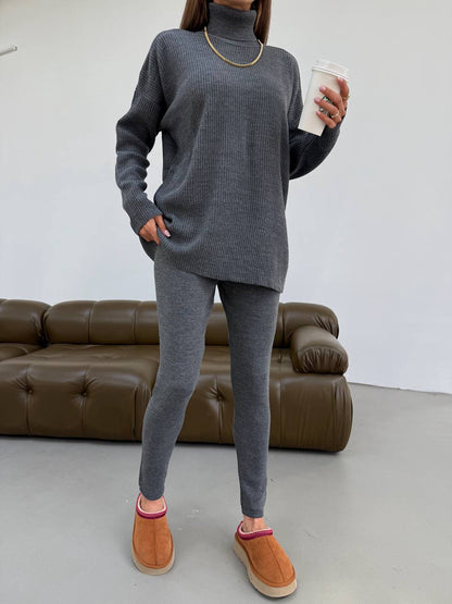 Person wearing a gray sweater and leggings set with brown shoes, holding a white cup indoors.