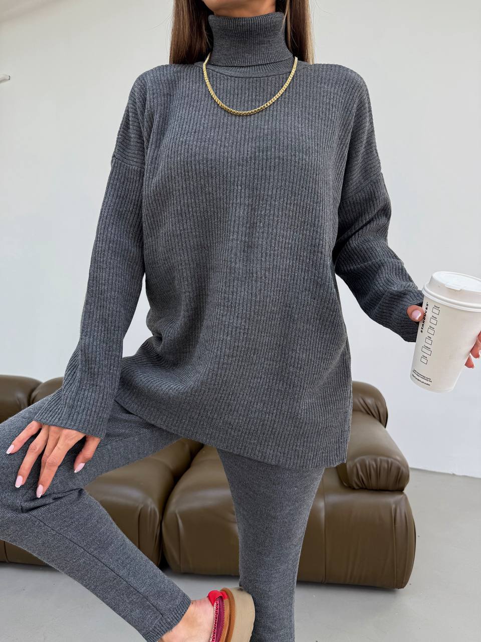 Person wearing a gray sweater and leggings holding a coffee cup indoors.