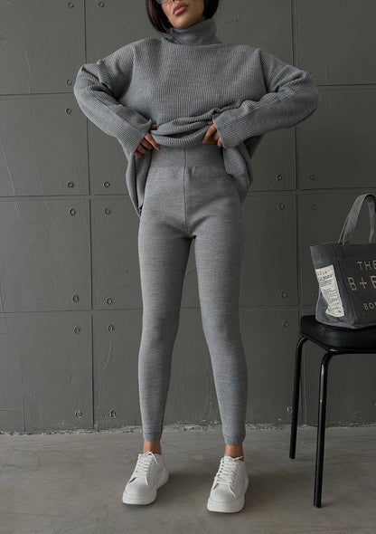 Person wearing a gray knit outfit with white sneakers in a minimalistic setting.