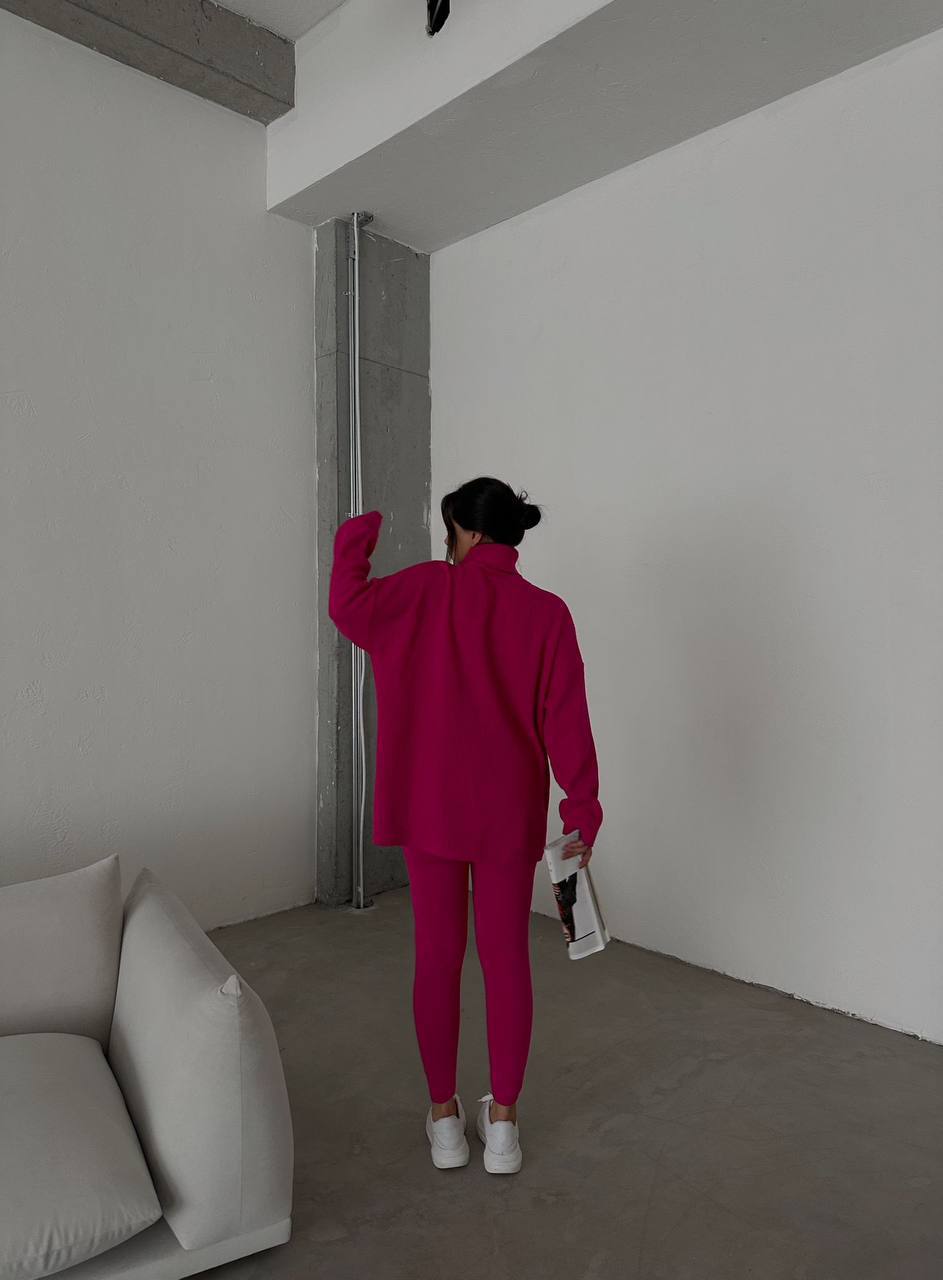 Person in a bright pink outfit standing in a minimalistic room with a white couch.