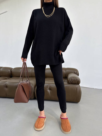 Person wearing a black outfit with brown shoes and a brown bag, standing in front of a brown sofa.
