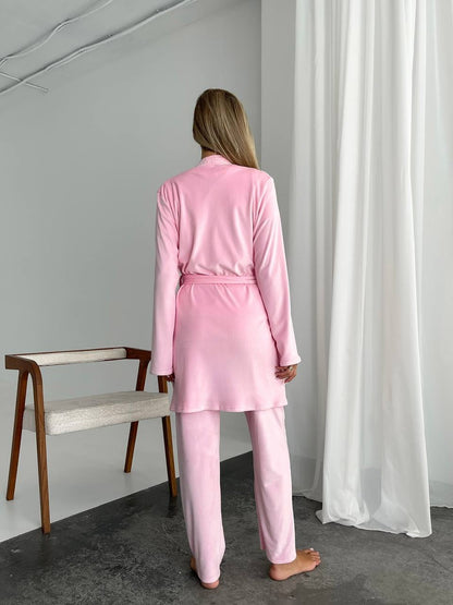 Person wearing a pink pajama set standing in a room with a chair and white curtains.