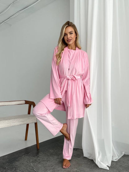 Woman wearing a pink robe and pants in a room with a bench and white curtains.