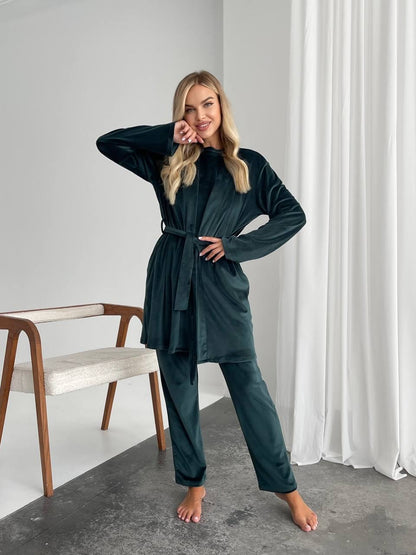 Woman wearing a dark green outfit in a minimalistic room with a chair and white curtain.