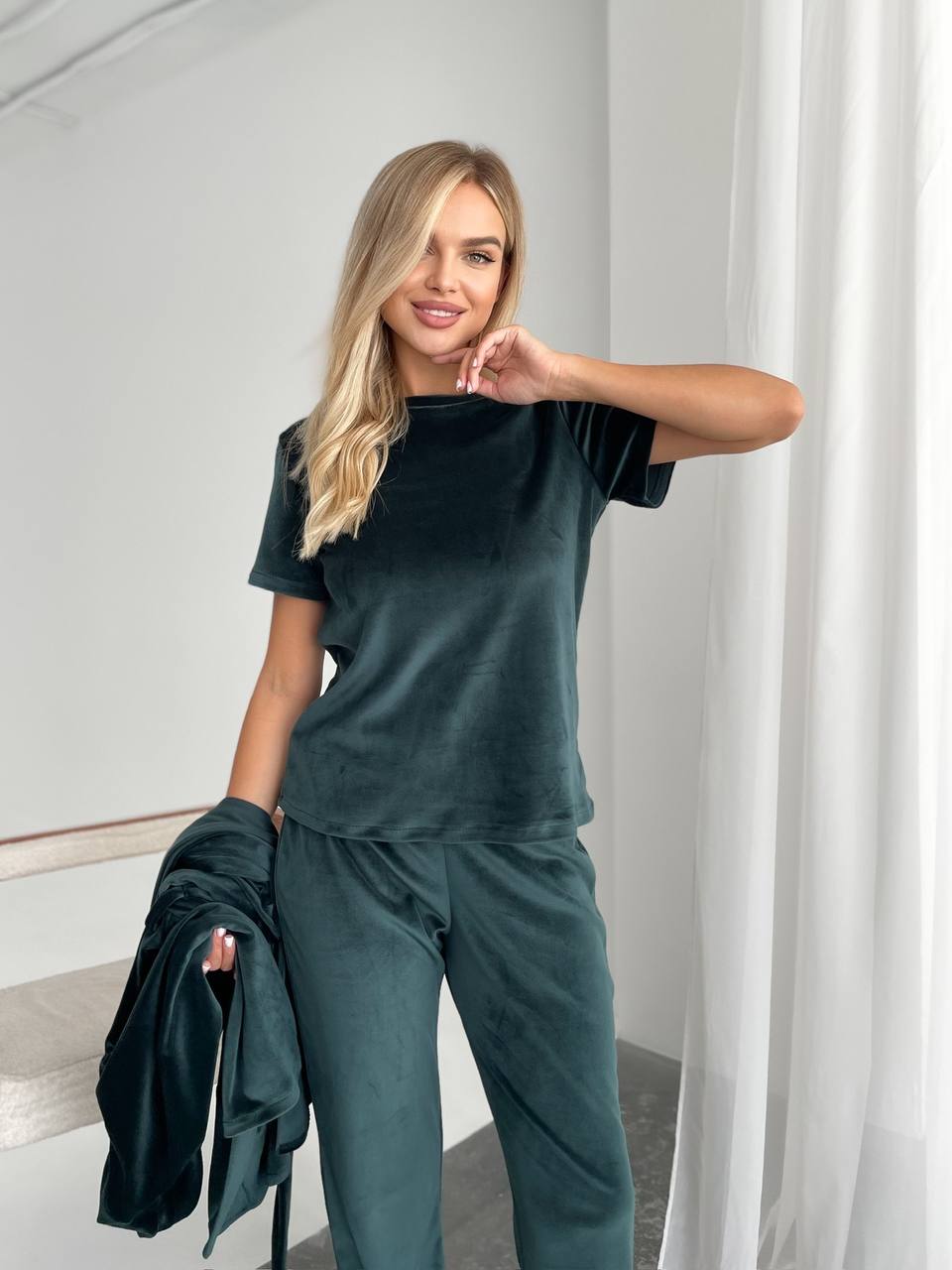 Woman wearing a dark green outfit in a minimalistic room.