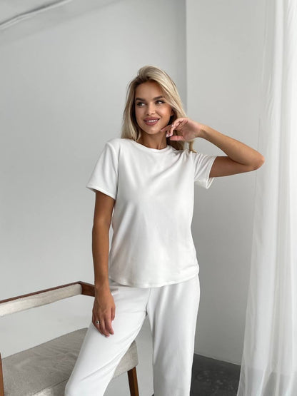 Woman wearing a white outfit sitting on a chair against a plain background