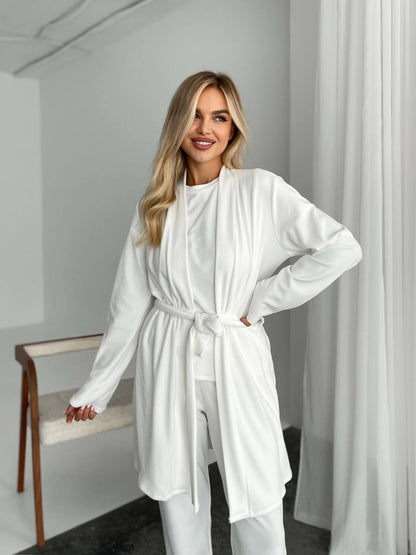 Woman wearing a white outfit in a minimalistic room with a chair and curtains.
