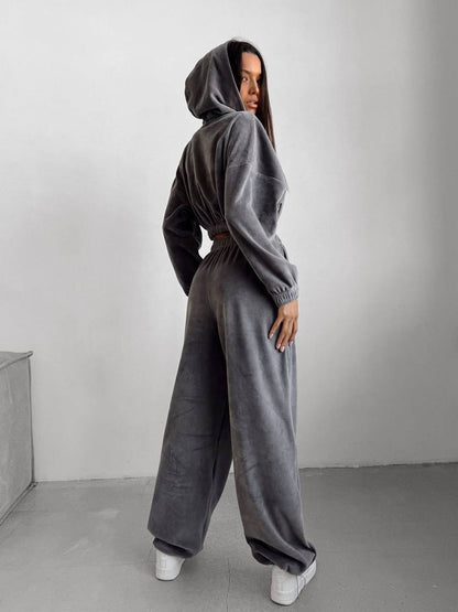 Person wearing a gray hoodie and wide-leg pants against a plain background