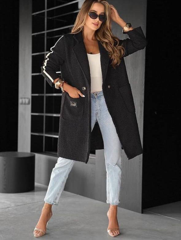 Woman wearing a black coat and light blue jeans in an indoor setting
