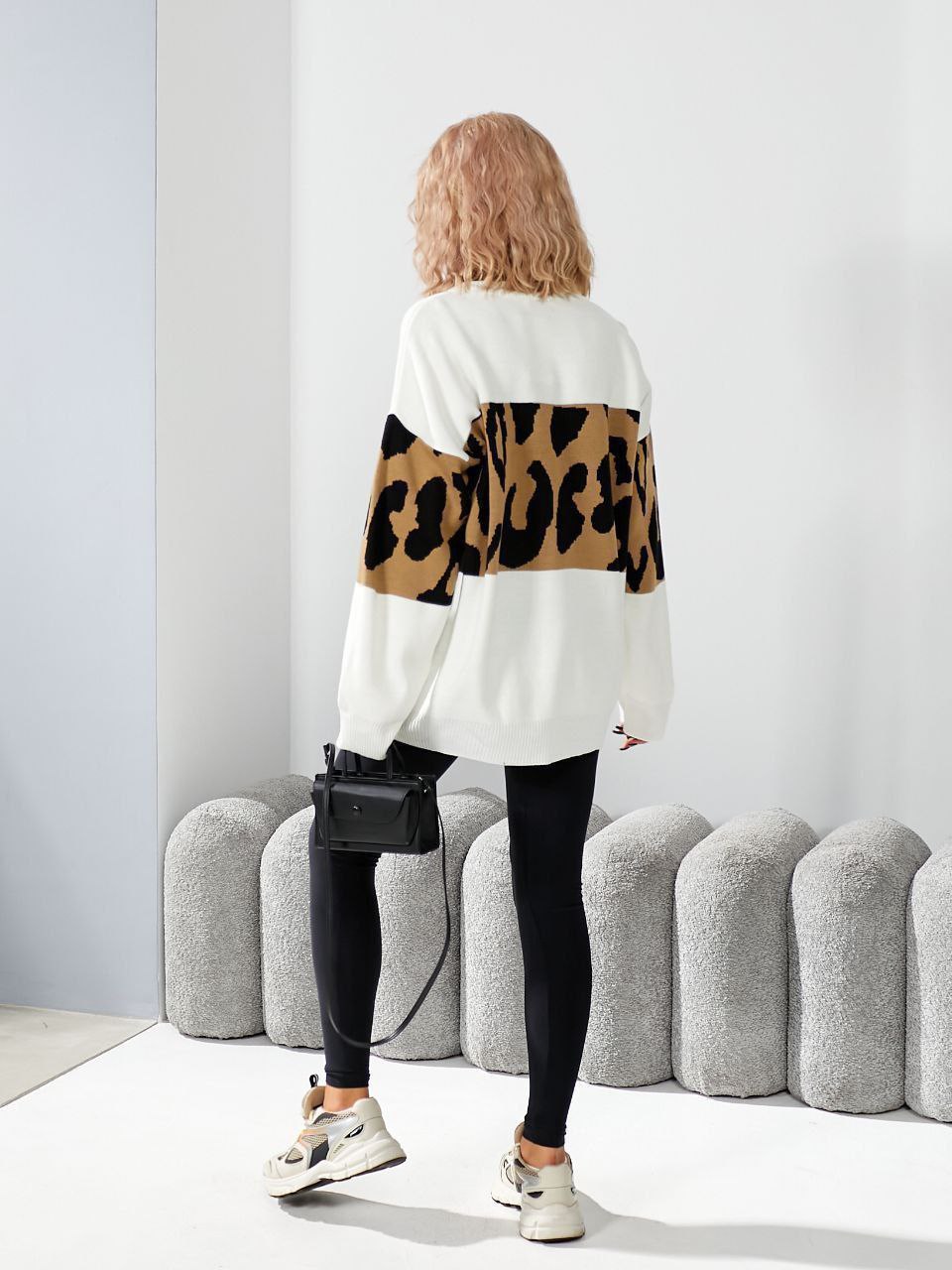 Person wearing a white sweater with leopard print sleeves in a minimalistic setting.