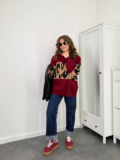 Woman wearing a red sweater with leopard print sleeves, blue jeans, and red sneakers in a room.