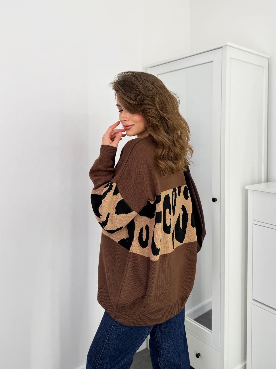 Woman wearing a brown sweater with leopard print sleeves in a room.