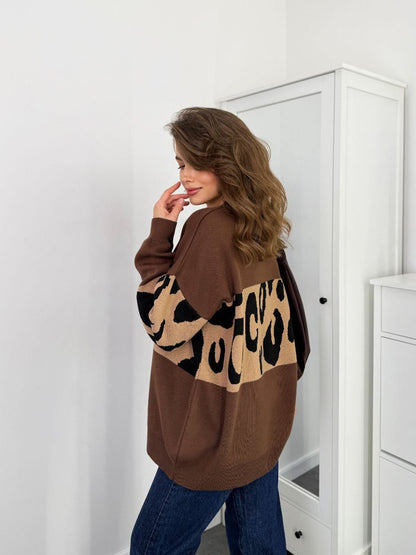 Woman wearing a brown sweater with leopard print sleeves in a room.