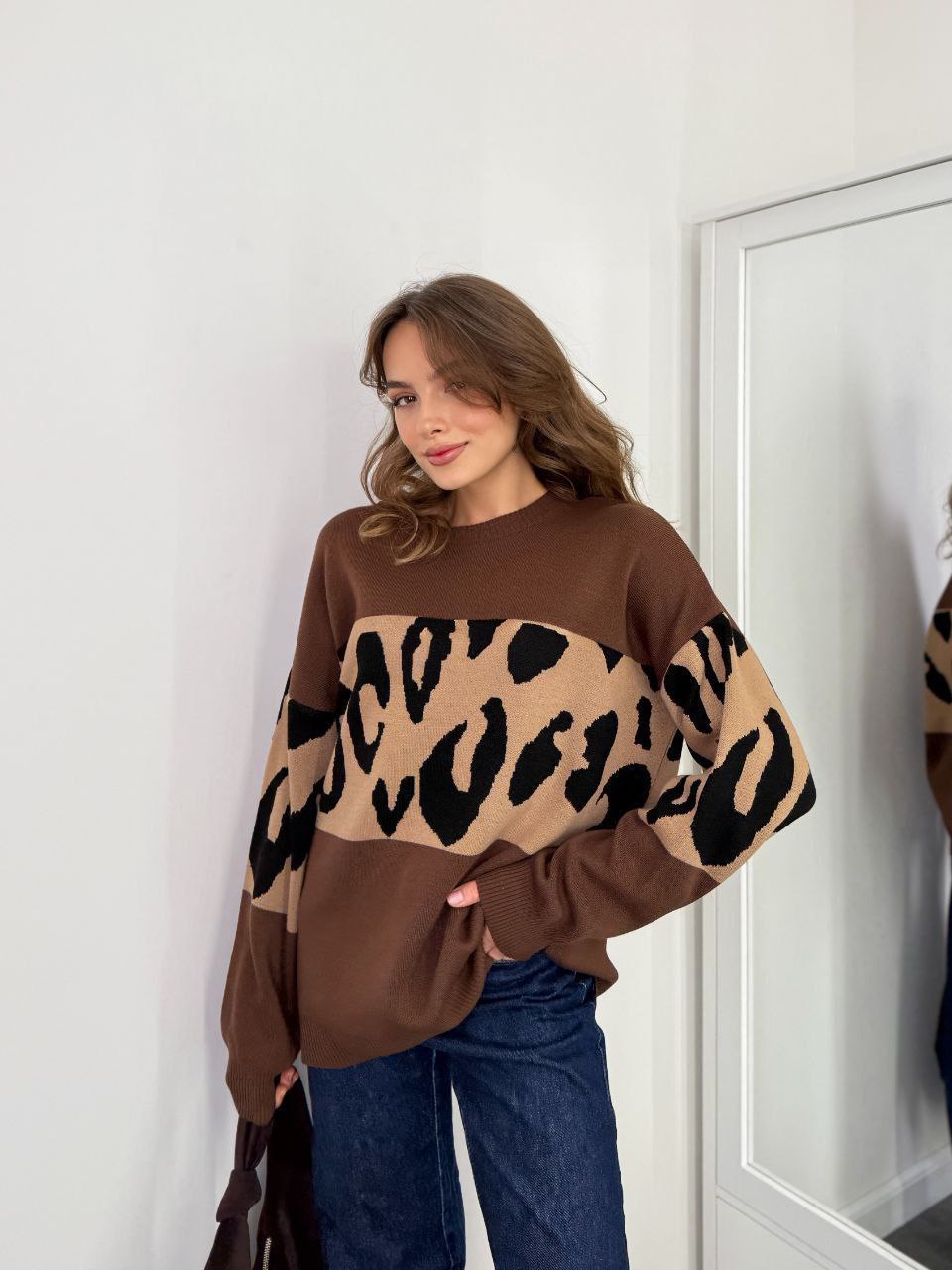 Woman wearing a brown sweater with leopard print sleeves standing in front of a mirror.