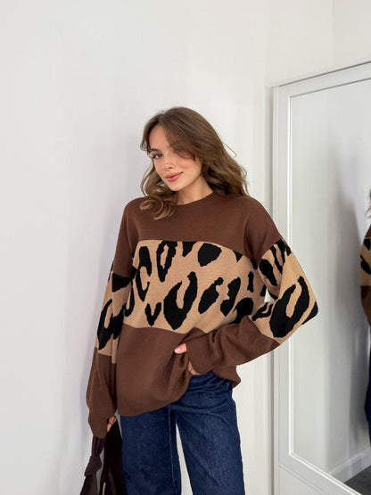 Woman wearing a brown sweater with leopard print sleeves standing in front of a mirror.