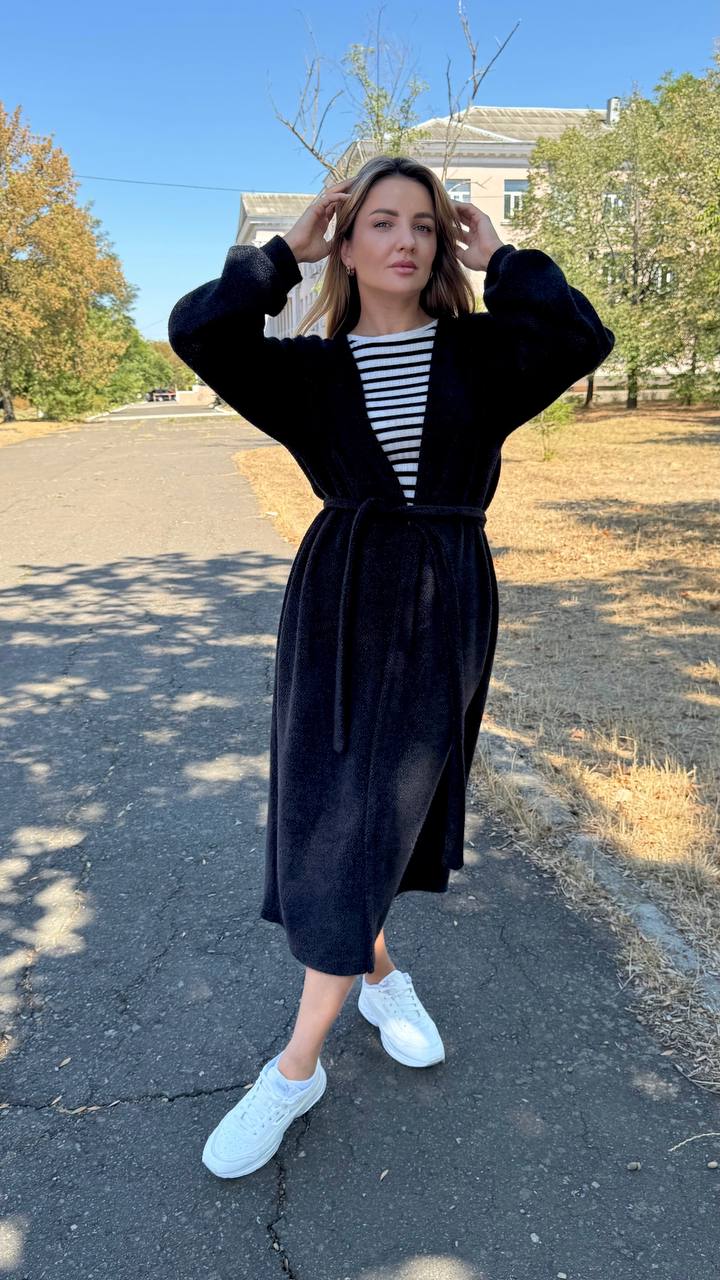 Woman in a black coat and striped shirt standing on a road with trees in the background