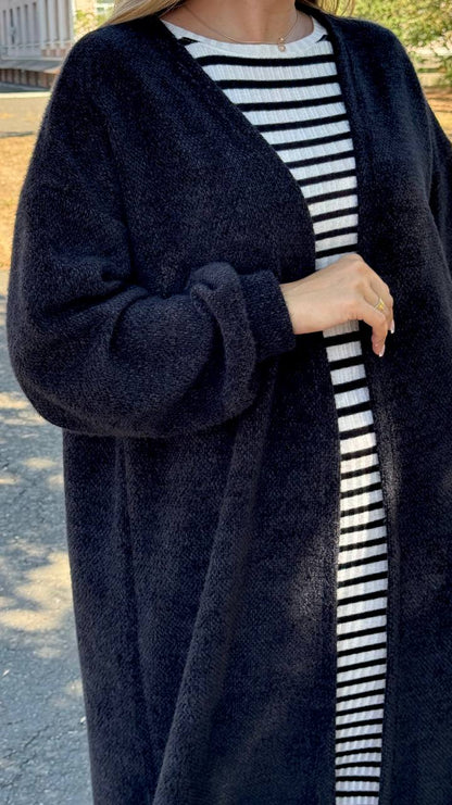 Person wearing a long dark blue cardigan over a striped shirt outdoors.