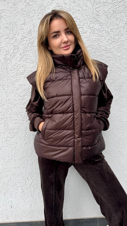 Woman wearing a brown puffer jacket against a textured white wall