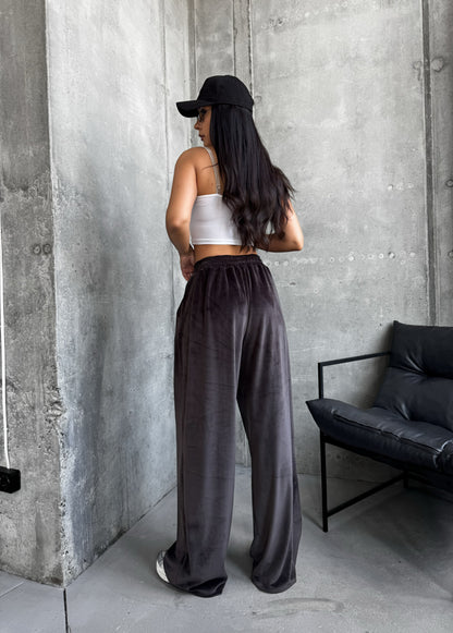 Woman wearing a white top and dark pants standing against a concrete wall.