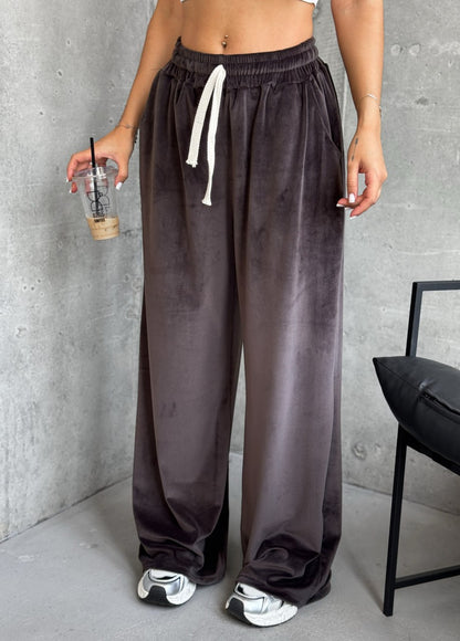 Person wearing brown wide-leg pants with a gray wall and chair in the background