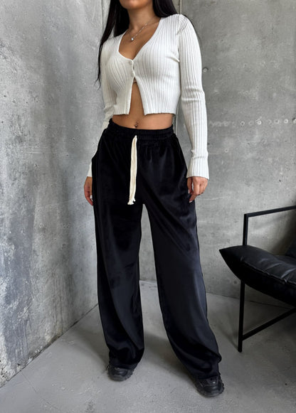 Person wearing a white cropped sweater and black pants against a gray concrete wall.