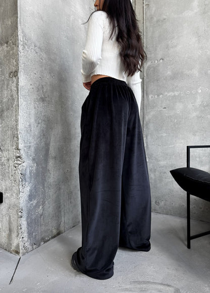 Person wearing a white top and black wide-leg pants standing against a concrete wall.