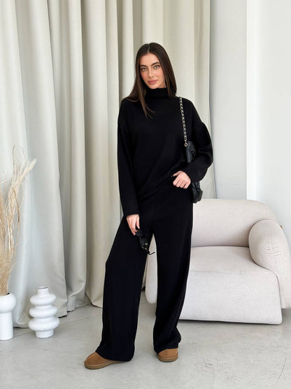 Woman in a black outfit standing in a minimalistic room with white curtains and a white sofa.