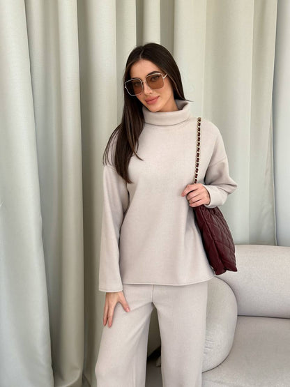 Woman in a light gray outfit holding a brown bag against a white curtain background