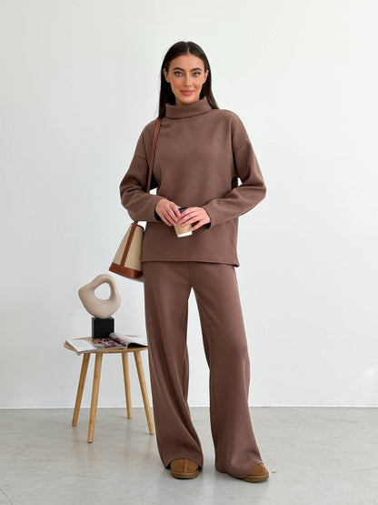 Woman wearing a brown outfit standing next to a chair with a bag on it against a white background