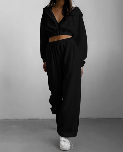 Person wearing a black outfit with a hood against a gray background