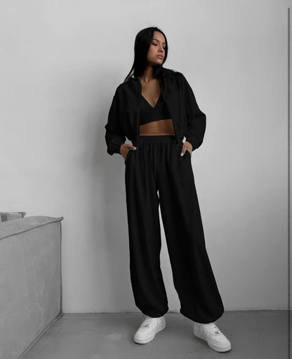 Person wearing a black outfit with white sneakers in a minimalistic setting