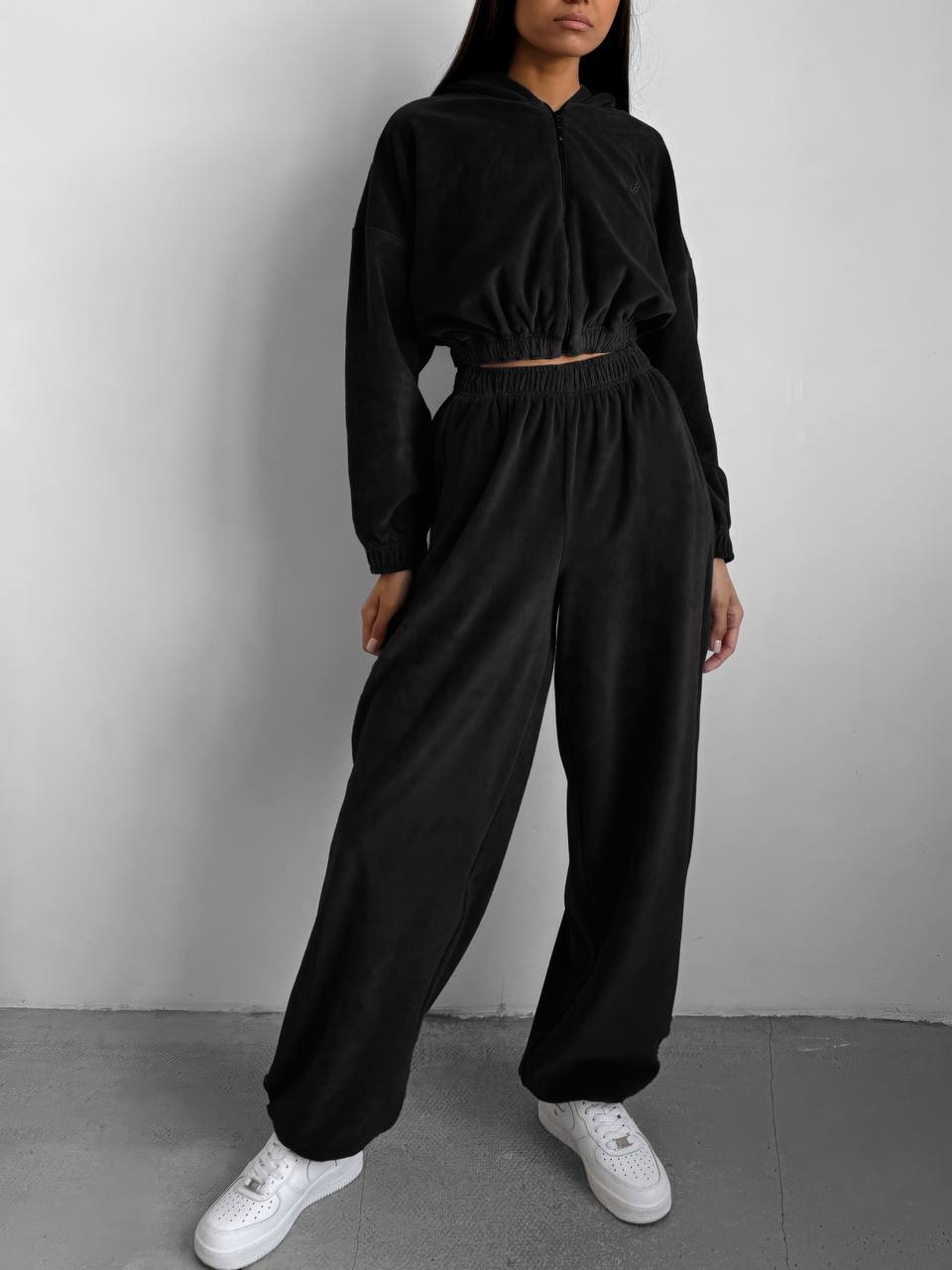 Person wearing a black outfit with white sneakers on a plain background