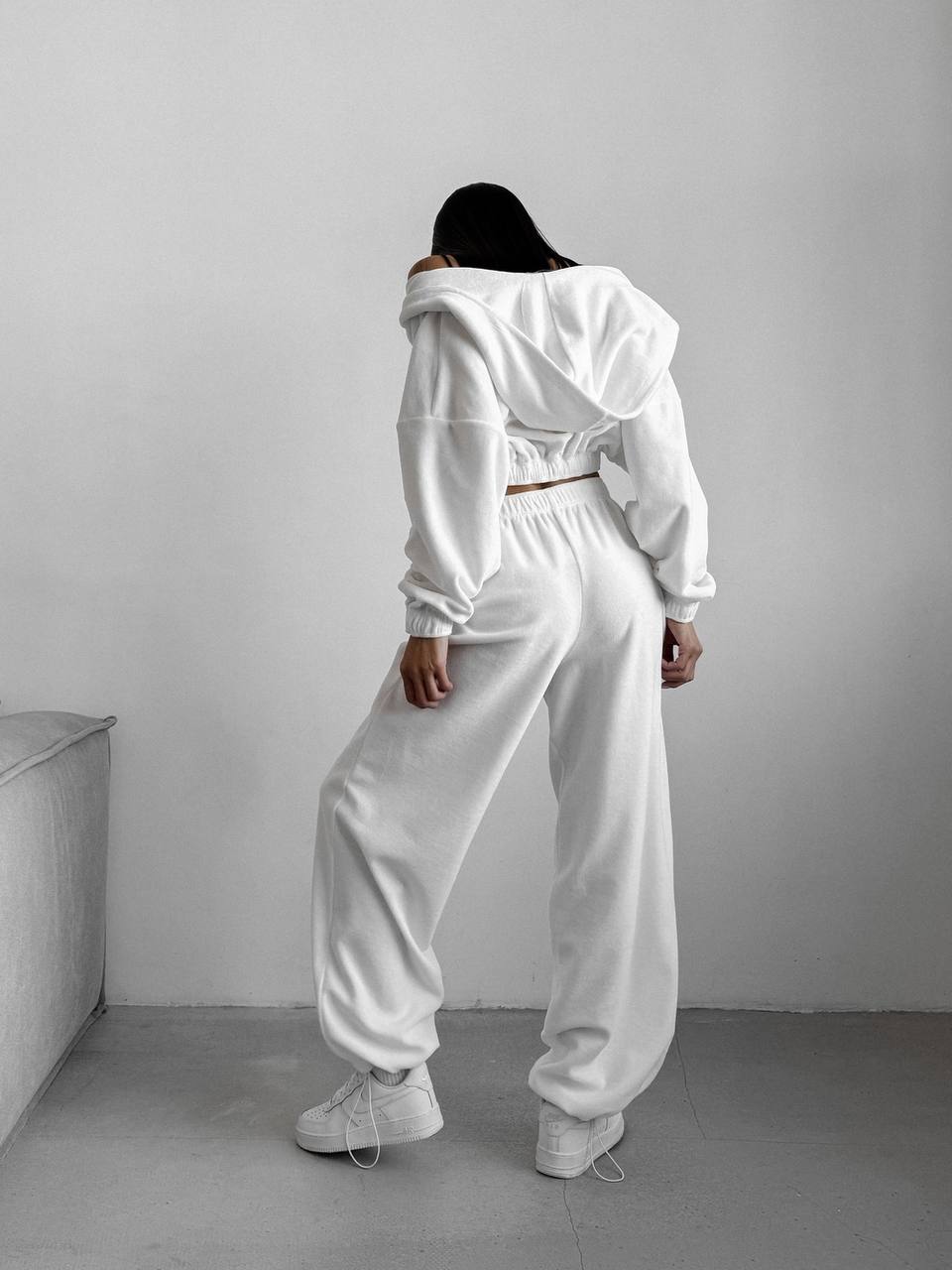 Person wearing a white tracksuit standing against a plain wall.