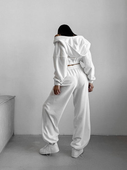 Person wearing a white tracksuit standing against a plain wall.