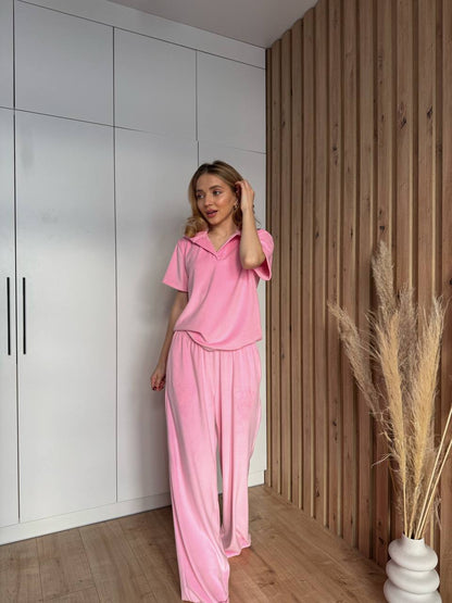 Woman in pink outfit standing in a room with white walls and wooden paneling.