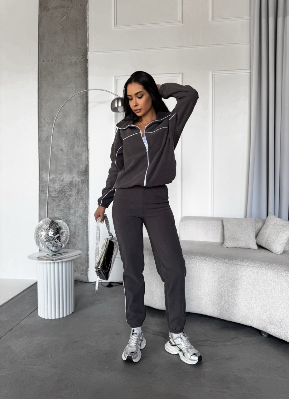 Woman in a dark gray tracksuit standing in a modern living room.