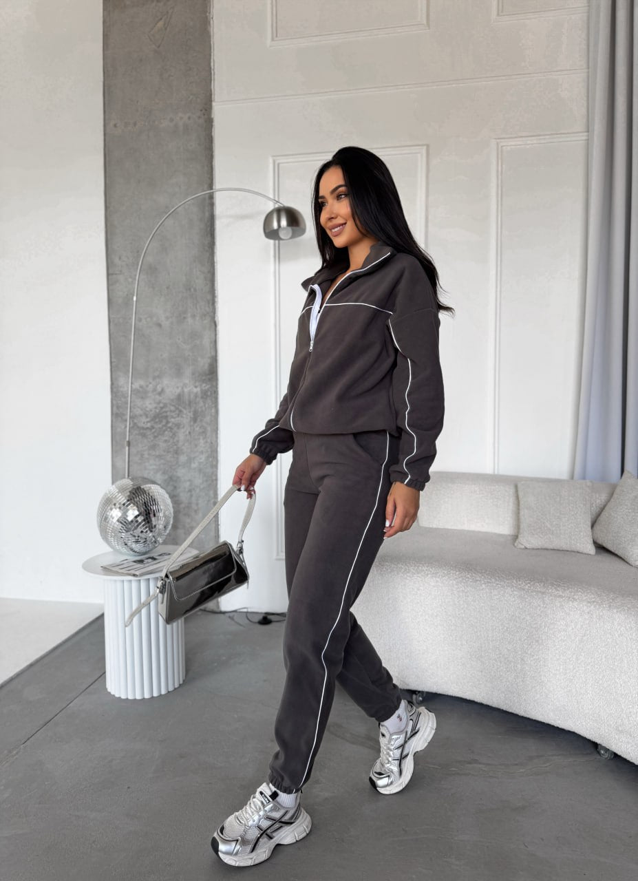 Woman in a dark gray tracksuit standing in a modern living room.