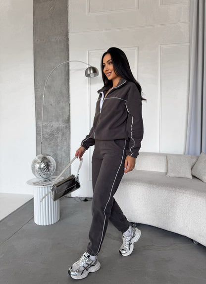 Woman in a dark gray tracksuit standing in a modern living room.