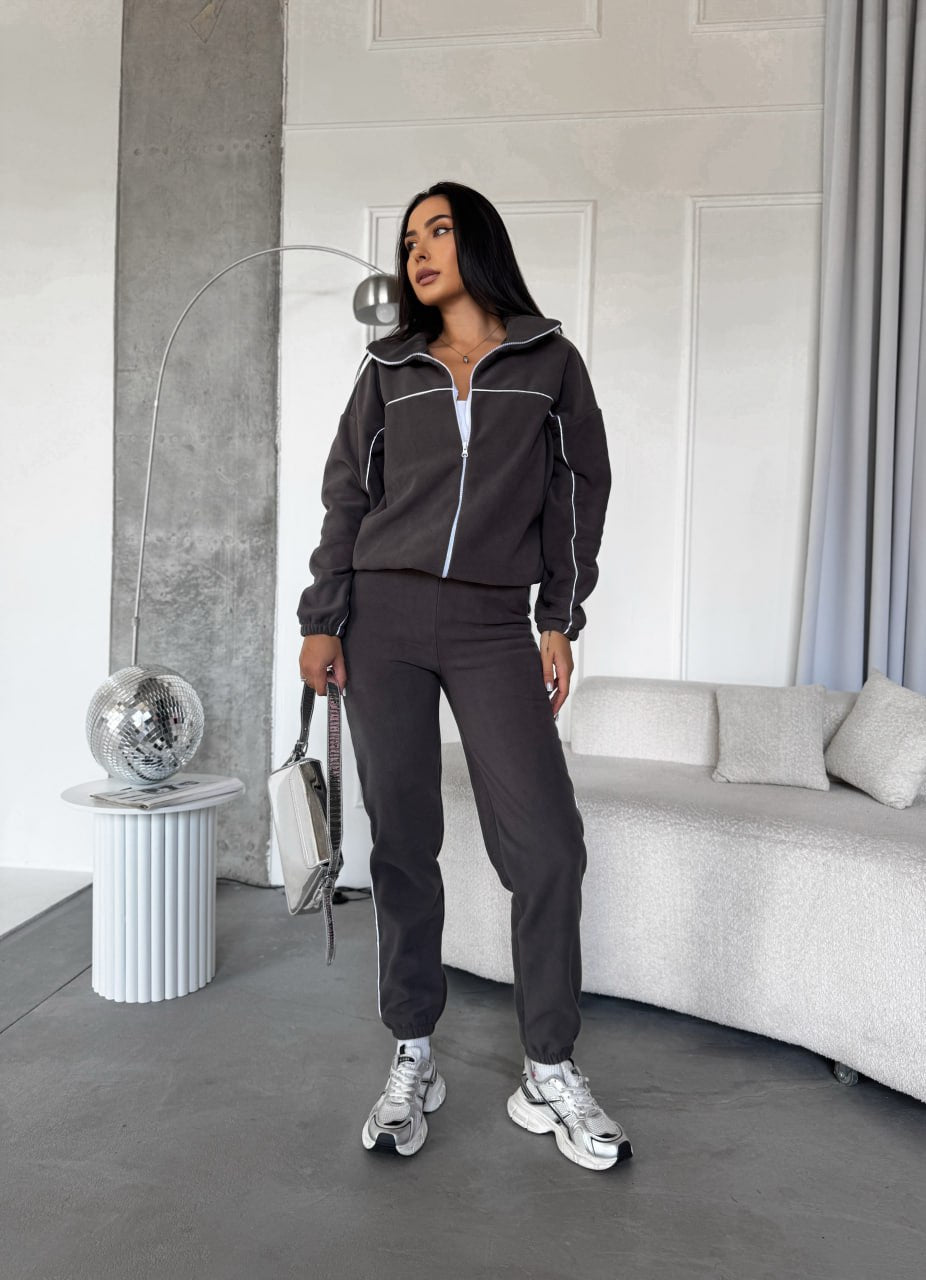 Woman in a dark gray tracksuit standing in a modern living room.