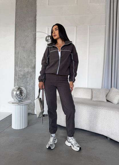 Woman in a dark gray tracksuit standing in a modern living room.