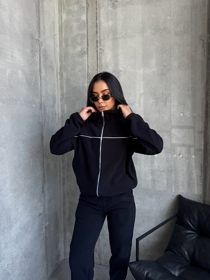 Person wearing a black tracksuit against a gray concrete wall.