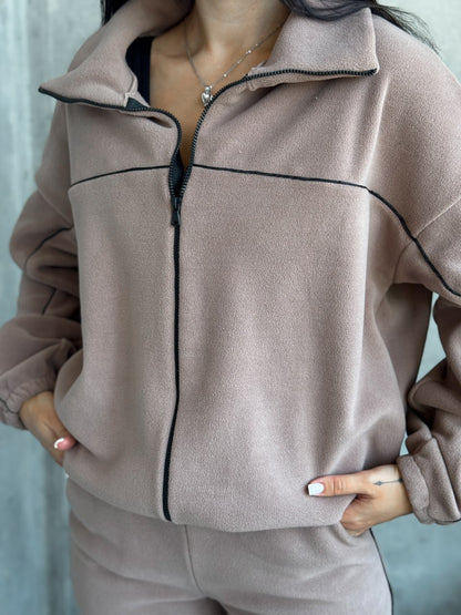 Person wearing a beige tracksuit with black piping against a light blue background